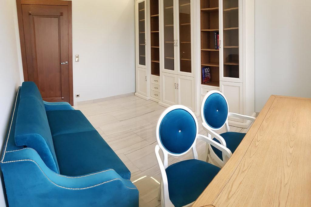 Projekt wnętrza gabinetu w stylu klasycznym - niebieska kanapa tapicerowana tkaniną, biała biblioteczka, białe krzesła z niebieskim siedziskiem i oparciem